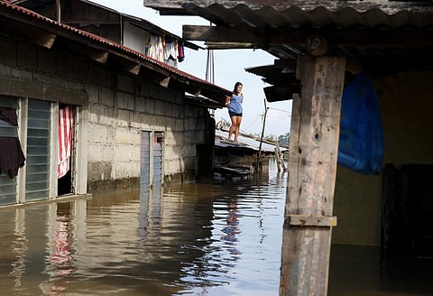 In this Monday, Sept. 17, 2018 file photo, a resident stands on the roof of her house amidst flooding brought about by Typhoon Mangkhut which barreled into northeastern Philippines during the weekend and inundated low-lying areas in its 900-kilometer wide