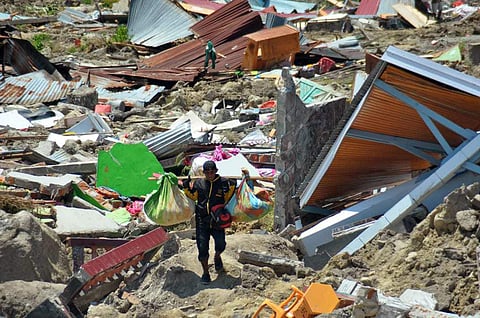 A man carry items he saved from the rubble following a major earthquake and tsunami in Palu, Central Sulawesi, Indonesia, Monday, Oct. 1, 2018. A mass burial of earthquake and tsunami victims was being prepared in a hard-hit city Monday as the need for he