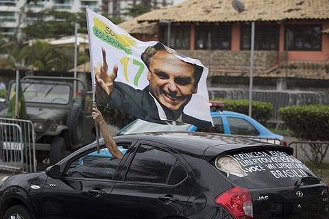 A supporter waves a flag with an image of Jair Bolsonaro as he drives past in front of his residence in Rio de Janeiro, Brazil | AP