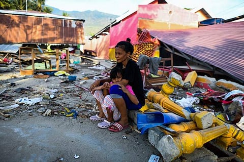 An earthquake-affected woman and her child sit amongst the rubble of their collapsed house on the outskirts of Palu in Indonesia's Central Sulawesi on October 5, 2018, following the September 28 earthquake and tsunami. Search teams made desperate last-dit