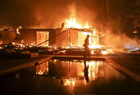 A firefighter walks by the a burning home in Malibu, Calif., Friday, Nov. 9, 2018. A Southern California wildfire continues to burn homes as it runs toward the sea. Winds are blamed for pushing the fire through scenic canyon communities and ridgetop homes