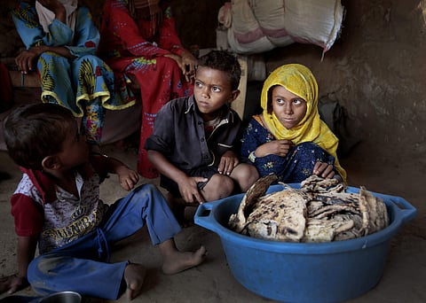 ​In this Oct. 1, 2018, photo, children sit in front of moldy bread in their shelter, in Aslam, Hajjah, Yemen. In a plastic washtub, the children's mother collects hard bread crumbs even those covered with mold, then mix with water, add salt, and give to h