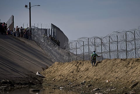 Migrants, top left, speak with U.S. border agents standing on the other side of razor wire near the Chaparral border crossing, seen from Tijuana. (Photo | AP)