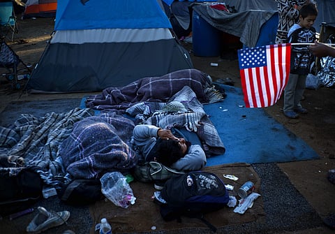 A migrant holding a U.S. flag, right, speaks with others waking up at the Benito Juarez Sports Center that's serving as a temporary shelter in Tijuana, Mexico. ( Photo | AP)