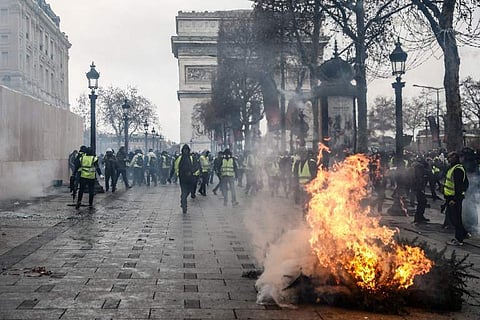 Protesters wearing yellow vests (gilets jaunes) stand next to a burning tree, as they demonstrate against rising costs of living they blame on high taxes near the Arc de Triomphe on the Champs-Elysees avenue in Paris. (Photo | AFP)