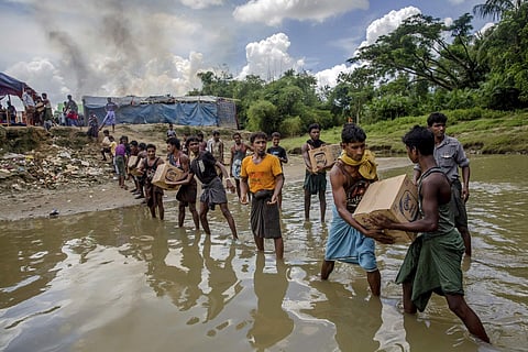 In this Sept. 15, 2017 file photo, Rohingya Muslims carry food items across from Bangladesh towards no man's land where they have set up a refugee camp, as smoke rise from fire across the border in Myanmar, in Tombru. (Associated Press)