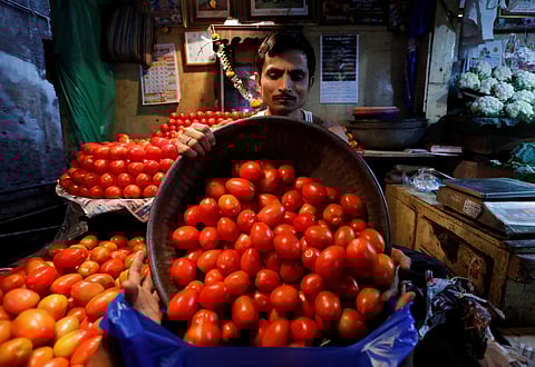 A vendor loads tomatoes in a bag for a customer at a wholesale vegetable market in Mumbai | Reuters