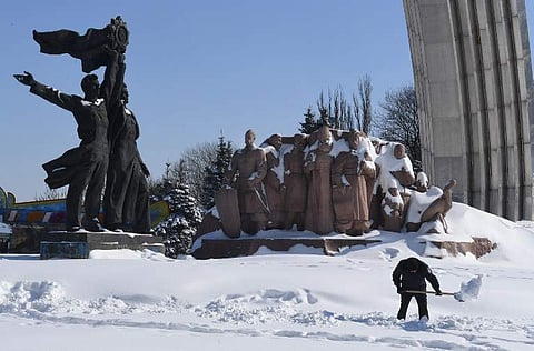 A communal worker cleans a road from a snow in front of Soviet era monument Ukraine and Russia union in Ukrainian capital of Kiev after heavy night snowfall on March 2, 2018 | AFP