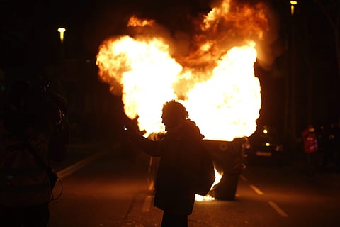 A man stands in front of a burning trash container during a protest after the detention of deposed leader of Catalonia's pro-independence party Carles Puigdemont in Barcelona. | AP