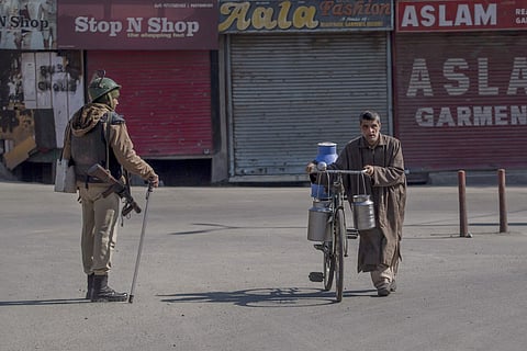 Kashmiri milk man walks his bicycle past an Indian paramilitary soldier during restrictions in Srinagar. | AP