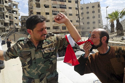 A man kisses his national flag which is wrapped around the arm of a Syrian soldier, after Syrian police units entered the town of Douma, the site of a suspected chemical weapons attack and the last rebel-held town | AP
