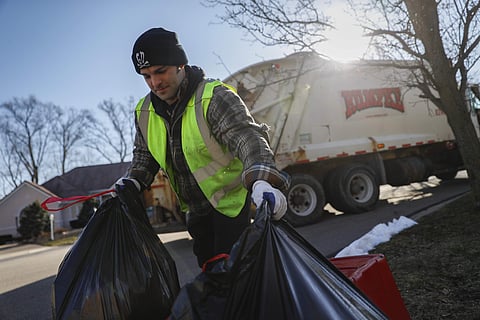 In this March 23, 2018, photo, trainee Brent Cottongin, with Rumpke Waste & Recycling, hauls recycling bags as he works a residential route in Beavercreek, Ohio. | AP