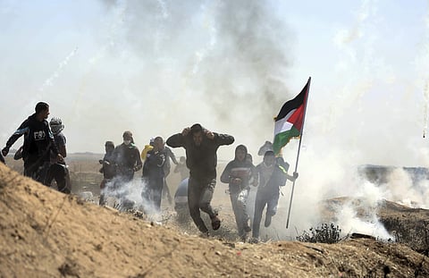 Palestinian protesters run for cover from teargas fired by Israeli troops during a protest at the Gaza Strip's border. (FILE | AP)