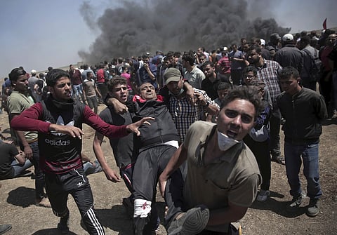 Palestinian protesters carry an injured man who was shot by Israeli troops during a deadly protest at the Gaza Strip's border with Israel | AP