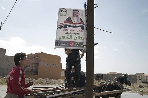 Iraqi teens make a team effort of removing an election campaign poster to retrieve the frame to sell as scrap metal, a day after parliamentary elections in Mosul, Iraq. | AP