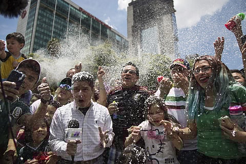 A reporter and fans are covered in foam during the celebration of Mexico's 2018 World Cup win over Germany at the Angel of Independence in Mexico City, Sunday, June 17, 2018. | AP