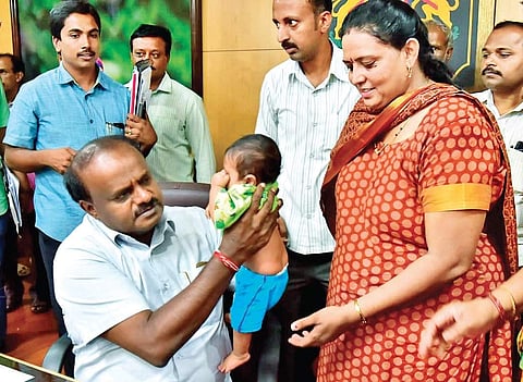 H D Kumaraswamy carries the child of Shyla who had come from Davanagere, during his Janata Darshan programme on Thursday | Express