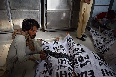 A Pakistani man sits next to a relative's dead body after a bomb blast at a election rally, at a hospital in Quetta. (Photo | AFP)