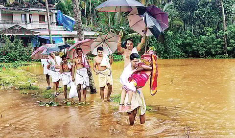 An acolyte helps Vedan, the little Karkkidaka Theyyam, cross an inundated field in Madhur, Kasargod on Friday | RaNju gnf