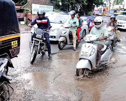 Motorists trying to negotiate the waterlogged pothole  at Alinchuvadu