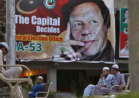 Pakistanis chat while they sit on a bench next to a big poster of Imran Khan, head of Pakistan Tehreek-e-Insaf party, at a market in Islamabad. (Photo | AP)