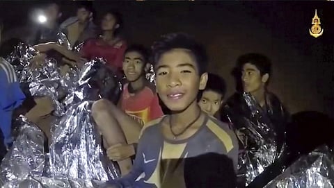 In this July 3, 2018, file image taken from video provided by the Royal Thai Navy Facebook Page, the boys smile as Thai Navy SEAL medic help injured children inside a cave in Mae Sai, northern Thailand. The group was discovered July 2 after 10 days totall