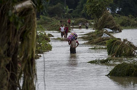 Residents walk on road submerged by flood waters from Swar Chaung Dam in Swar township in Bago region. (Photo | AFP)