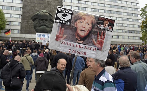 A protestor holds a poster with a photo of Angela Merkel reading 'Merkel must go' and referring she is guilty of incitement in Chemnitz, eastern Germany. (Photo | AP)