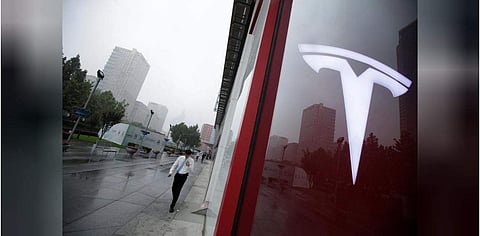 A man walks near a logo of Tesla outside its China headquarters at China Central Mall in Beijing (Photo | Reuters)