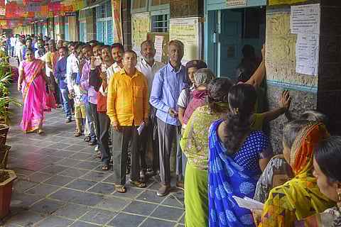 Voters stand in a queue as they wait to cast their votes at a polling station for the Maharashtra Assembly elections in Karad. (Photo | PTI)