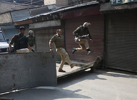 A policeman jumps as his officer kicks to remove a road block put up by protesters in Srinagar (Photo| AP)