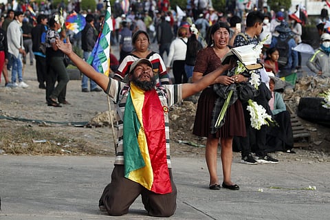 A coca leaf producer kneels holding a bible with his arms outspread asking police to open the way so a march by backers of former President Evo Morales may continue to Cochabamba, Bolivia, Saturday. (Photo | AP)