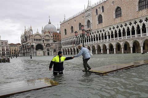 A city worker helps a woman who decided to cross St. Mark square on a gangway, in spite of prohibition, in Venice, Italy, Sunday, Nov. 17, 2019. | (Photo | AP)