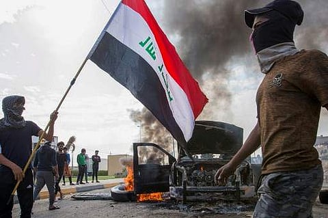 Iraqi demonstrators stand next to the smoking remains of an Iraqi anti-riot vehicle during a demonstration. ( File Photo | AFP)