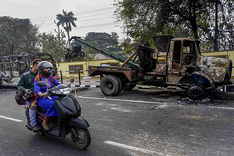 A scooterist rides past charred vehicles which were allegedly set on fire by the protestors during protests against the Citizenship Amendment Bill in Guwahati. (Photo | PTI)