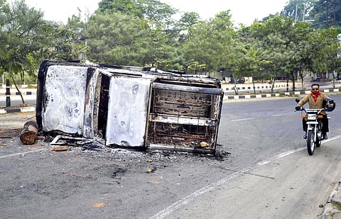 A man rides past a torched vehicle set on fire by anti-CAB protestors at Bamunimaidam in Guwahati. (Photo | PTI)