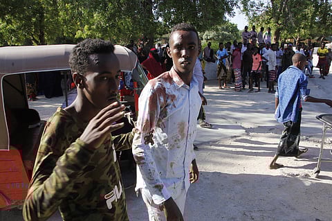 A civilian who was wounded in suicide car bomb attack is helped by a friend at check point in Mogadishu, Somalia, Saturday, Dec, 28, 2019. A police officer says a car bomb has detonated at a security checkpoint during the morning rush hour in Somalia's ca