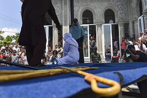 People watch as an Indonesian woman is whipped by a member of the Sharia police in public in Banda Aceh. (Photo | AFP)