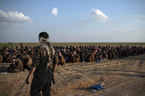 FILE - In this Friday, Feb. 22, 2019 file photo, U.S.-backed Syrian Democratic Forces (SDF) fighters stand guard next to men waiting to be screened after being evacuated out of the last territory held by Islamic State group militants, near Baghouz, easter