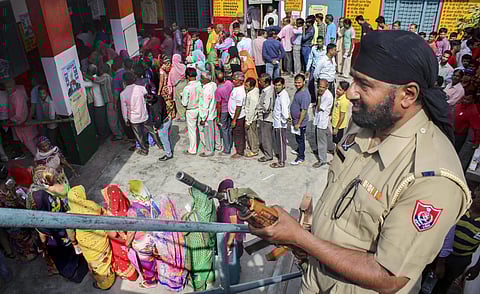 A  securityman stands guard as voters queue to cast their vote during the first phase of general elections at a polling station in Meerut. (Photo | PTI)