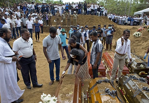 Anusha Kumari, center, holds a coffin during a mass burial for her husband, two children and three siblings, all victims of Easter Sunday's bomb blast in Negombo. (Photo | AP)