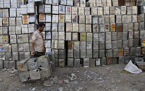 A man carries empty aluminium tins used for edible oil past a stack of tins at a recycling yard in Ahmedabad (File Photo | Reuters)