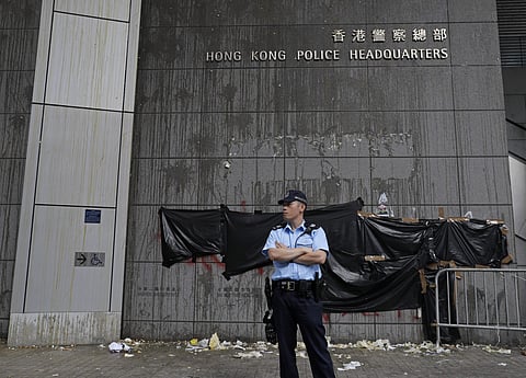 A police officer stands in front of a wall partly covered by plastic sheet as it was defaced by protesters at the main entrance of the police headquarters in Hong Kong. (Photo | AP)