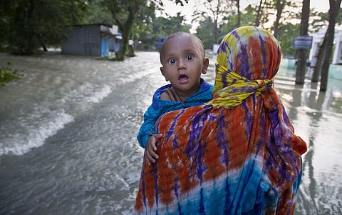 An woman carrying her child wades through a flooded road in Jhargaon, east of Gauhati, Assam. (Photo | AP)