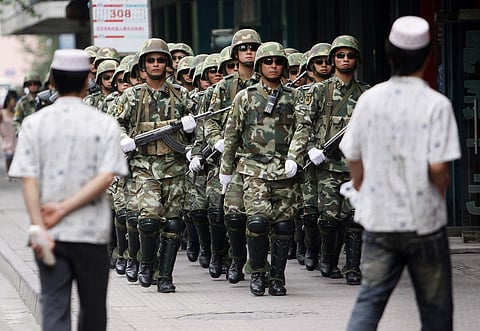 Paramilitary police officers patrol in the aftermath of riots as Uighur men walk by in Urumqi, western China's Xinjiang province on July 13, 2009 (File | AP)