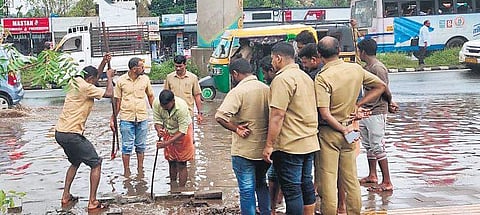 Autorickshaw drivers and Fire and Rescue Services personnel poke holes in the drain to clear water accumulated on the road near Kalamassery Metro Station |  Express