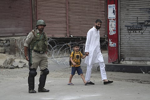 In this Friday, Aug. 30, 2019, file photo, a man walks with a child past an Indian paramilitary soldier standing guard during restrictions ahead of Friday prayers in Srinagar. | (File | AP)
