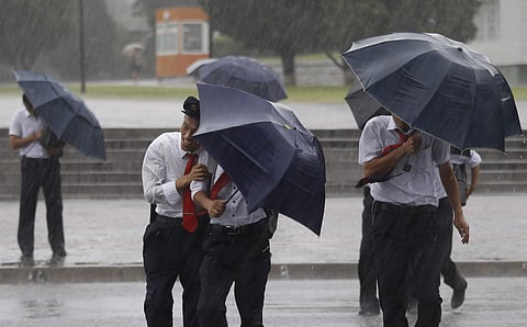 Pedestrians shield themselves from wind and rain brought by Typhoon Lingling. (Photo | AP)
