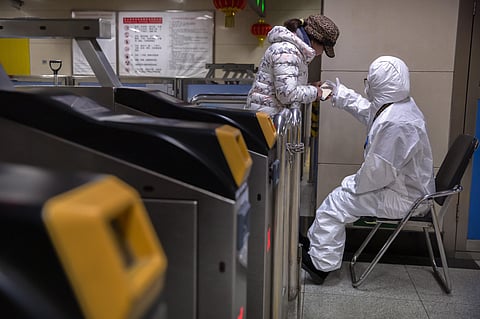 A worker wearing a hazardous materials suit gives directions to a passenger at a subway station in Beijing. (Photo| AP)