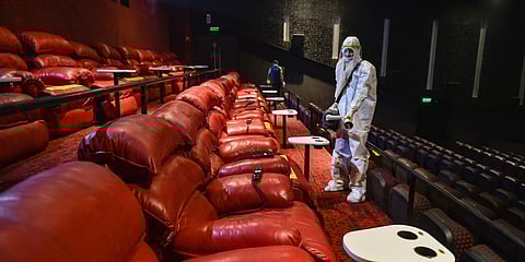 A worker wearing PPE kit sanitises a cinema hall as multiplexes prepare to re-open from October 15. (Photo| PTI)